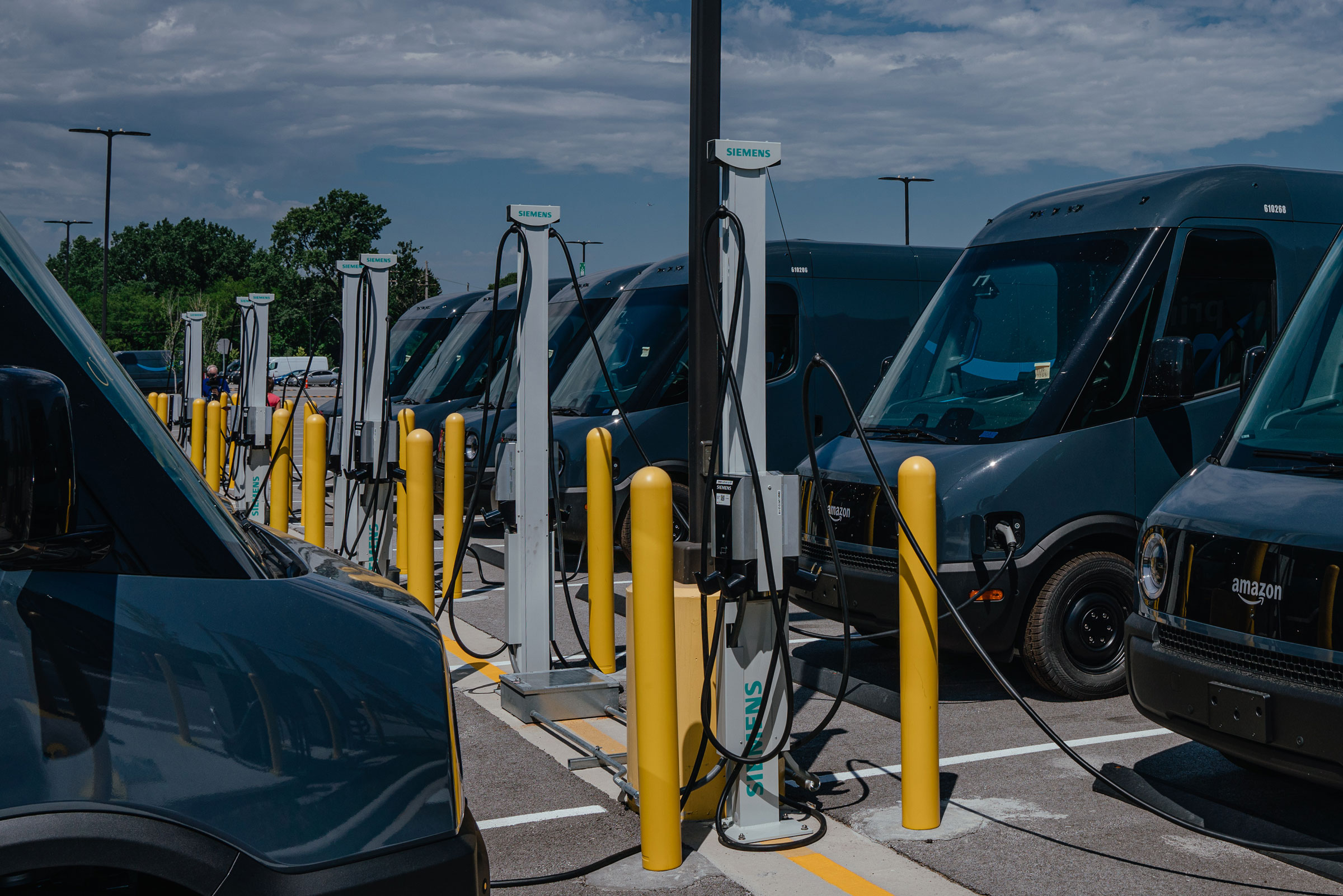Amazon delivery electric vans (EV), built by Rivian Automotive, at charging stations parked outside the Amazon Logistics warehouse in Chicago, Illinois on Thursday, July 21, 2022. Amazon Inc. is starting delivery of packages to US customers using the first of as many as 100,000 electric vans built by Rivian Automotive Inc., which aims to hand over thousands of the vehicles this year. (JAMIE KELTER DAVIS—BLOOMBERG/GETTY IMAGES)